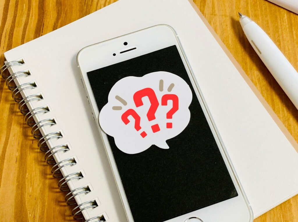 ノートに載ったスマホと赤い疑問符のイメージ